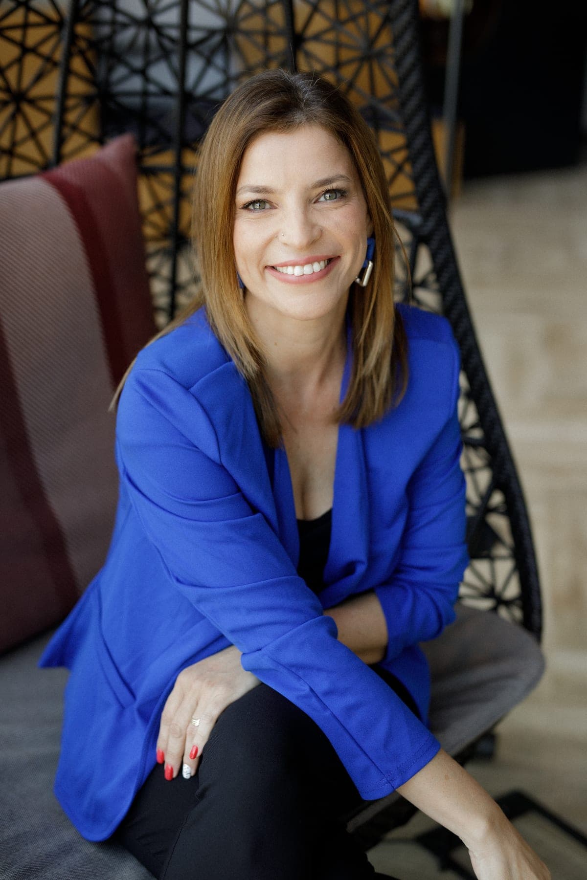 Ady Mor-Biran seated in a woven chair, leaning forward and smiling.